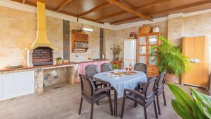 An outdoor dining area with a stone fireplace, a wooden cabinet with dishes, and a large potted plant. - Villa Gamor Frigiliana by Ruralidays (Málaga)