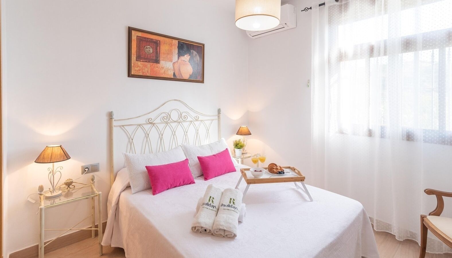 A neatly made bed with white and pink bedding, a tray with breakfast, and a painting on the wall.