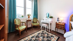 A hotel room with two green upholstered chairs, a white desk with a mirror, a small bedside table with a lamp, and a floral rug. - luxury studio 5 (Hlavní mesto Praha)