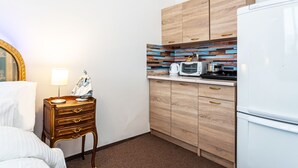 A compact hotel room with a wooden cabinet, a microwave, a refrigerator, and a bedside table with a lamp and a decorative item. - luxury studio 5 (Hlavní mesto Praha)