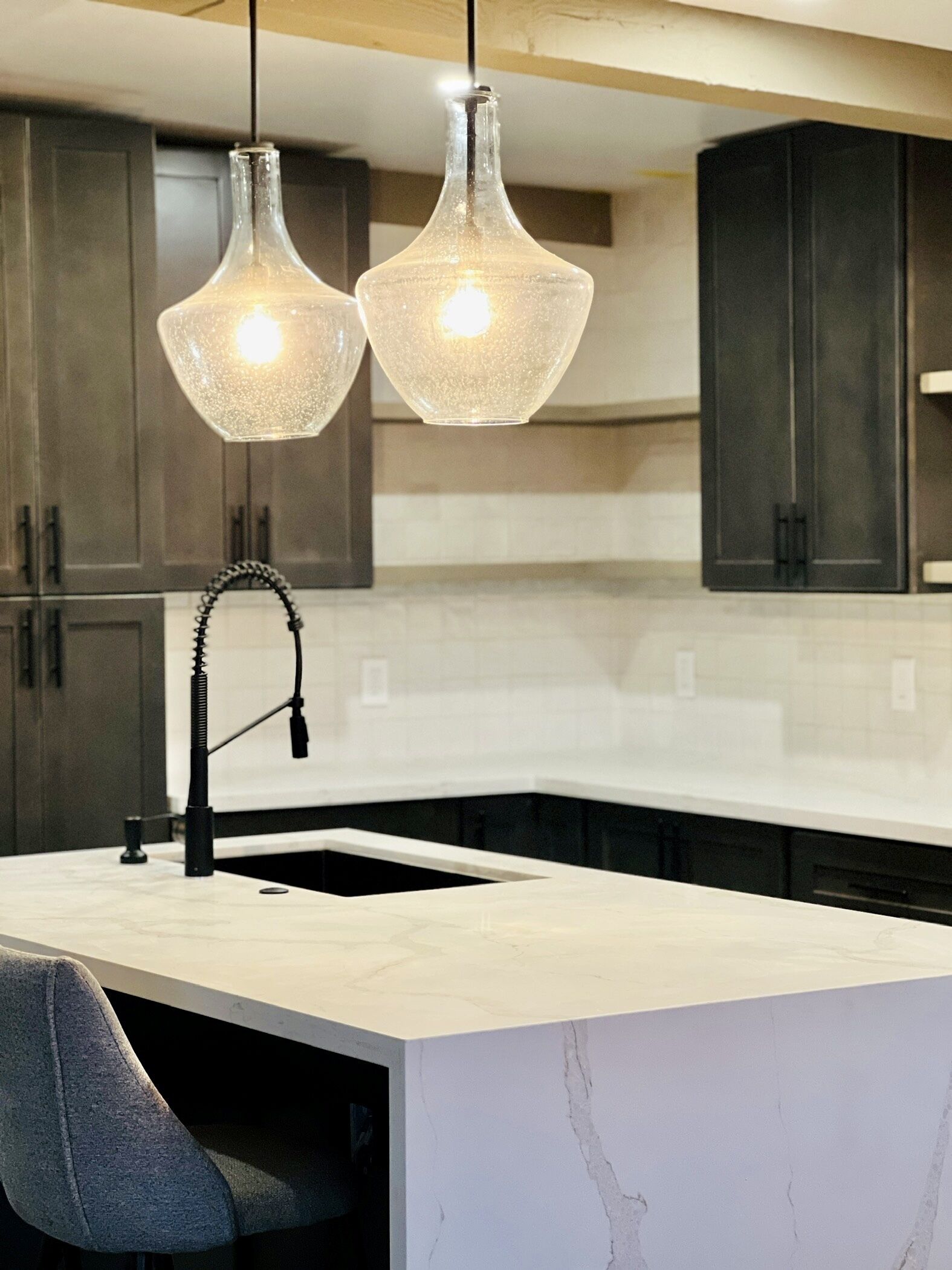 A kitchen with a marble countertop, a black faucet, and two hanging pendant lights.