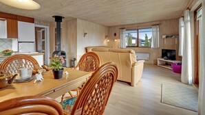 Een gezellig interieur van een chalet, met een eethoek, een bank, een televisie en een groot raam.