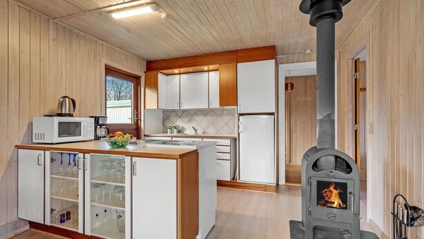 Een moderne keuken met witte kastjes, een magnetron, een spoelbak en een houtkachel.