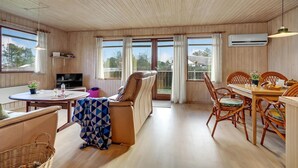Een gezellige kamer met een bank, een eettafel met stoelen, een televisie en grote ramen.