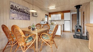 Een gezellige, goed verlichte kamer met een houten eettafel, rieten stoelen, een keuken met witte kastjes, een magnetron en een houtkachel.