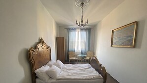 Ein Hotelzimmer mit einem grossen Bett, einer Kristallleuchter, einem Gemälde an der Wand und einer Sitzecke mit zwei Sesseln und einem Tisch.