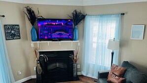 Un salon avec une cheminée, un téléviseur fixé au-dessus et un canapé agrémenté de coussins.
