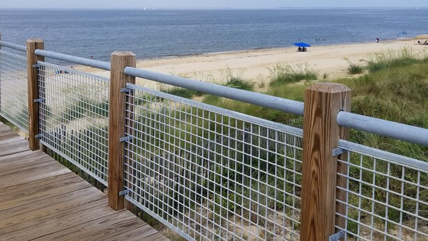 Une promenade en bois menant à une plage de sable, avec une clôture en métal et des poteaux en bois.