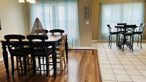 Un coin repas avec une table et des chaises en bois, un lustre et une vue dégagée à travers des rideaux légers.