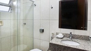 A bathroom with a glass shower enclosure, a white toilet, a granite countertop sink, and a mirror above the sink.
