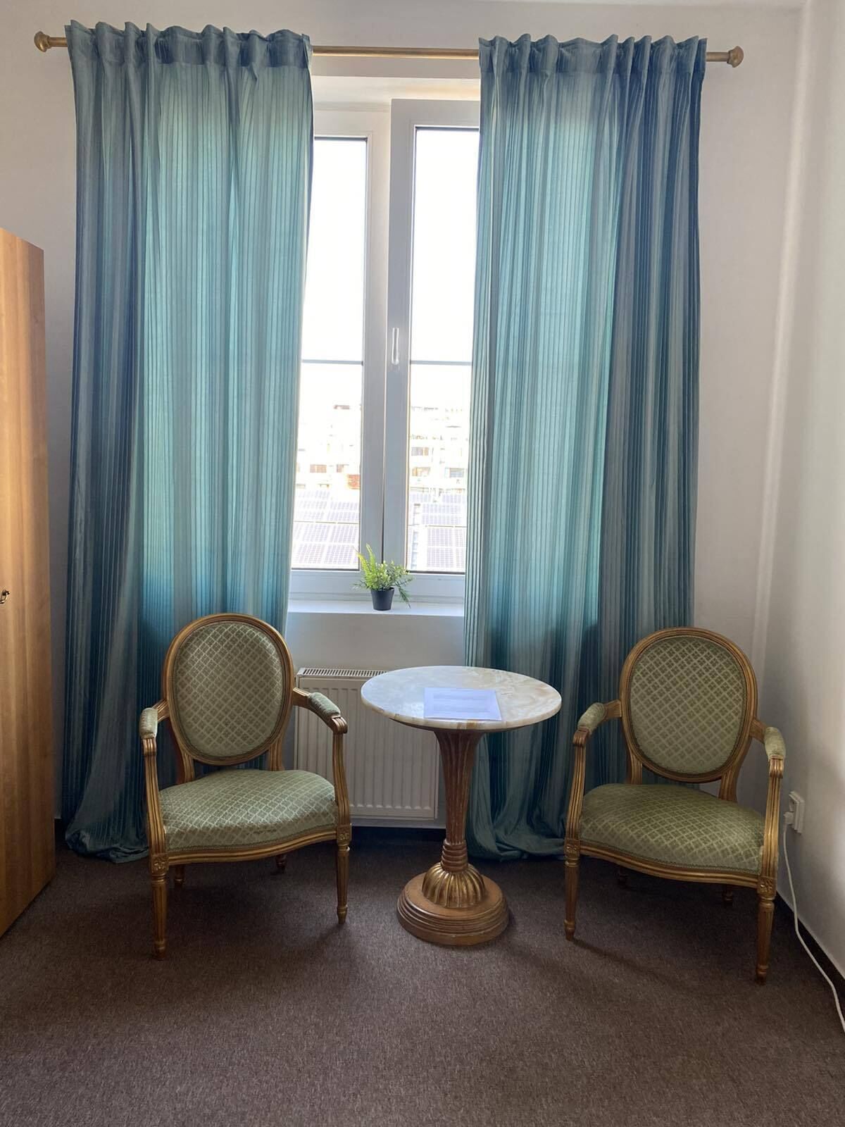 A room with two wooden chairs with cushioned seats and backs, a small round table, and a window with curtains.