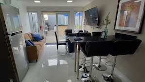 A modern kitchen with a refrigerator, a dining area with a table and chairs, and a sofa with blue cushions. - TURTUGA AT BIDA MARINO RESIDENCE (Noord)