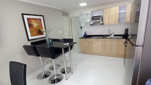 A modern kitchen with wooden cabinets, a black dining table with chairs, a microwave, and a refrigerator. - TURTUGA AT BIDA MARINO RESIDENCE (Noord)