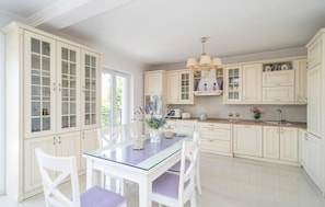 A spacious kitchen with white cabinetry, a glass-top dining table, and a chandelier.