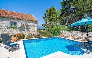 A swimming pool with lounge chairs and a stone building with a tiled roof.