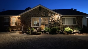 A stone house with a well-lit front porch, a driveway, and a landscaped front yard.
