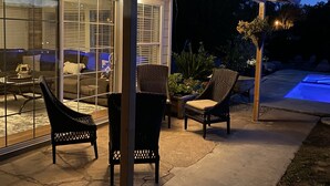 An outdoor patio area with a covered seating area, a pool, and potted plants.