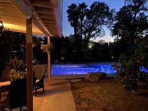 Zona de piscina exterior con un porche cubierto, mobiliario y vegetación circundante.