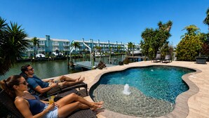 A pool area with lounge chairs, a water feature, and a marina in the background.