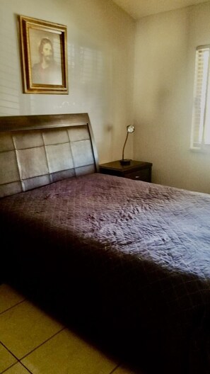 Ein Schlafzimmer mit einem Bett, einem Nachttisch, einem gerahmten Bild an der Wand und einem Fenster mit Jalousien.
