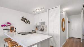 Une cuisine moderne avec des meubles blancs, un îlot en marbre doté de tabourets et des œuvres d’art décoratives sur les murs.