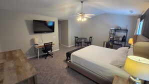 Ein Hotelzimmer mit Bett, Schreibtisch, Stuhl, Fernseher und Deckenventilator.