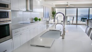 A modern kitchen with white cabinetry, stainless steel appliances, and a large window overlooking the ocean. - VillaPlayaEncantada-Pools&BeachAccess-Rosarito (Rosarito)