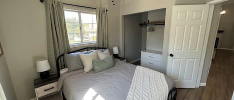A bedroom with a bed, nightstands, a window with curtains, a ceiling fan, and a door leading to another room.