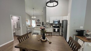 Una cocina moderna con armarios blancos, electrodomésticos de acero inoxidable y una zona de comedor con mesa y sillas de madera.