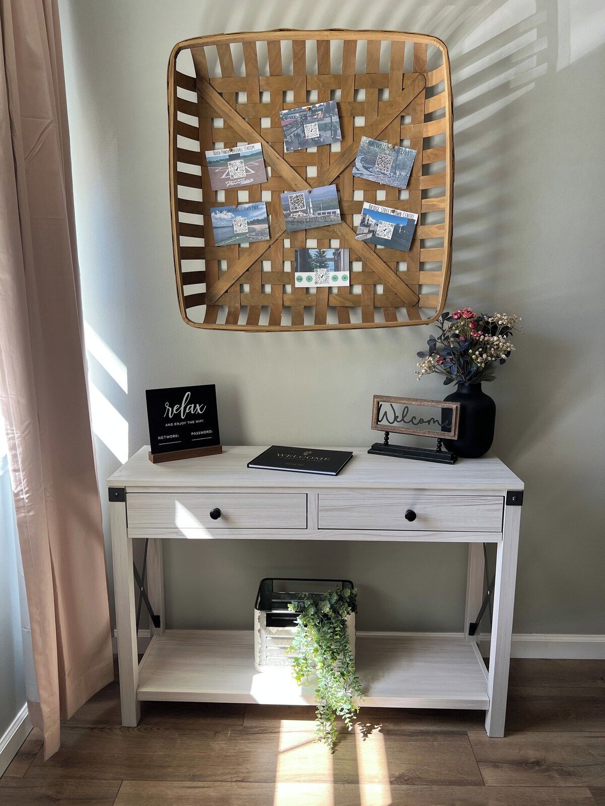 A white desk with a basket of printed photos, a welcome sign, a relaxation sign, and a small plant on a shelf.
