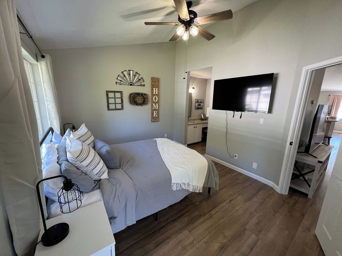 A bedroom with a bed, a ceiling fan, a TV, and a small desk.