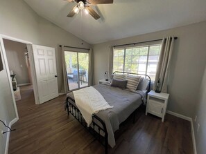 Une chambre à coucher avec un lit, des tables de chevet, un ventilateur de plafond et une vue sur l’extérieur par la fenêtre.