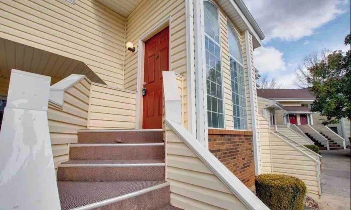 A residential building with a front porch, a red door, and a set of stairs leading to the entrance.