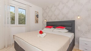 Ein ordentlich bezogenes Bett mit einer roten Rose und Handtüchern, ein Fenster mit transparenten Vorhängen und einer gemusterten Tapete.