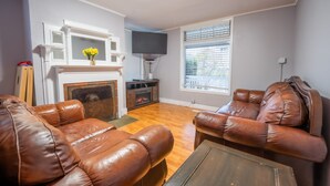 A living room with leather sofas, a fireplace, a flat-screen TV, and a window with blinds. - Top of Tacoma Flat Unit 1 (Tacoma)