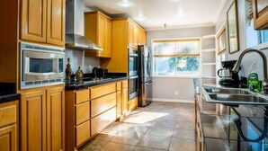 A modern kitchen with wooden cabinets, stainless steel appliances, and a large window providing natural light. - Top of Tacoma Flat Unit 1 (Tacoma)