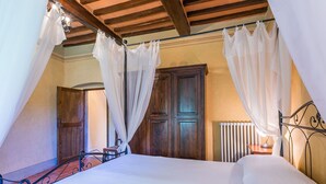Quarto com cama grande, vigas de madeira no teto e radiador.