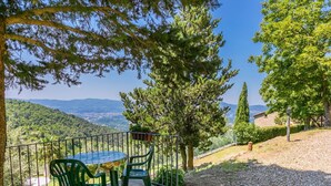 A terrace with a table and chairs, overlooking a scenic landscape with hills and a clear sky.
