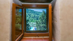 A corner of a room with a wooden ceiling and a window overlooking a forested hillside.
