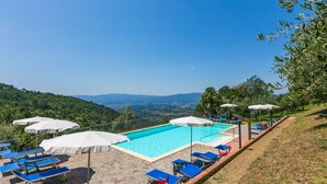A pool area with blue lounge chairs and white umbrellas, surrounded by a stone deck and overlooking a mountainous landscape. - Beautiful apartment for 6 people with WIFI, pool, TV, patio and panoramic view (Reggello)