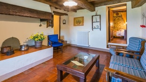 A rustic living room with exposed wooden beams, a blue chair, a plaid sofa, and a glass-top coffee table. - Beautiful apartment for 6 people with WIFI, pool, TV, patio and panoramic view (Reggello)