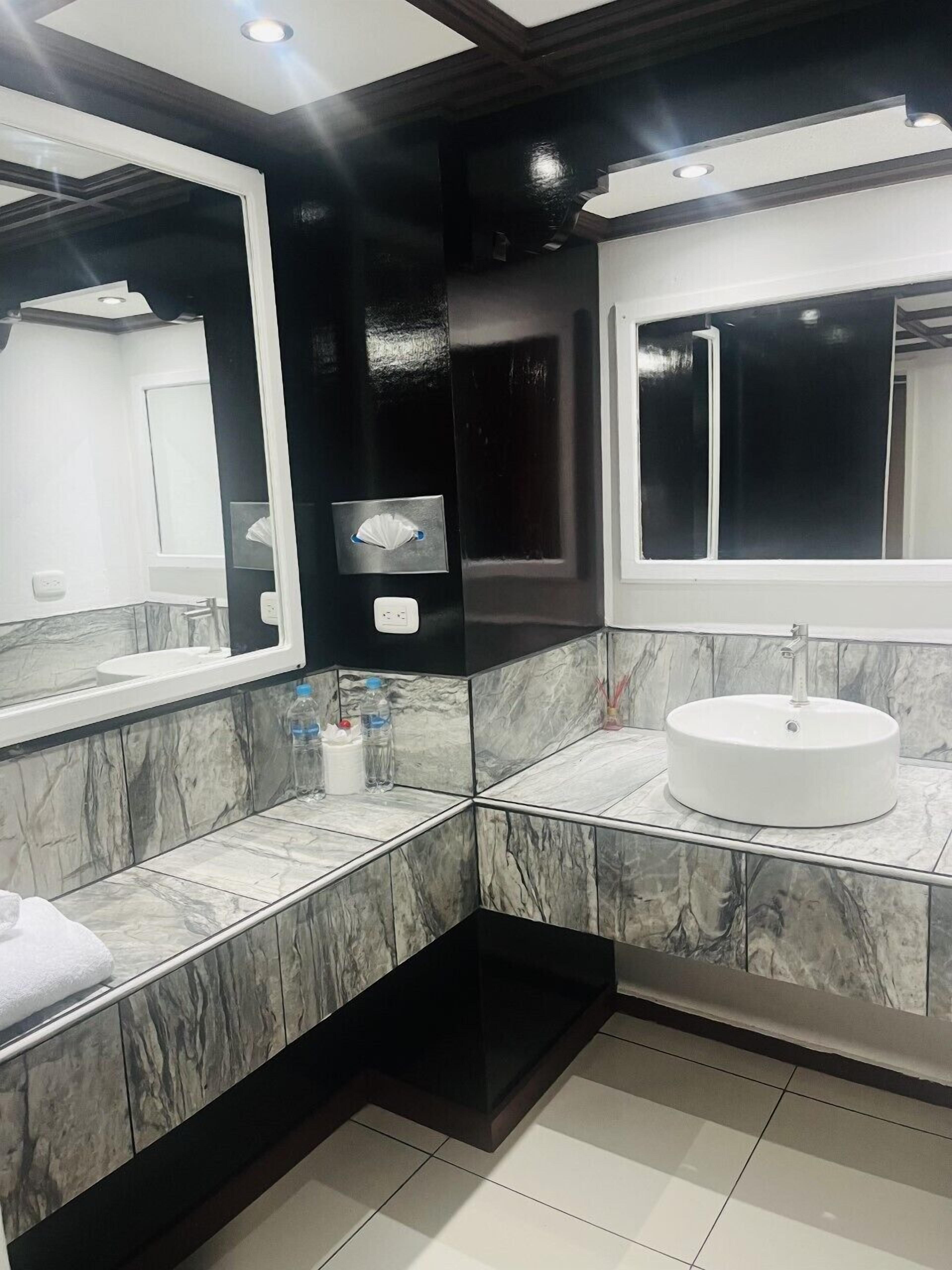 A modern bathroom with marble tiles, a round sink, and large mirrors.