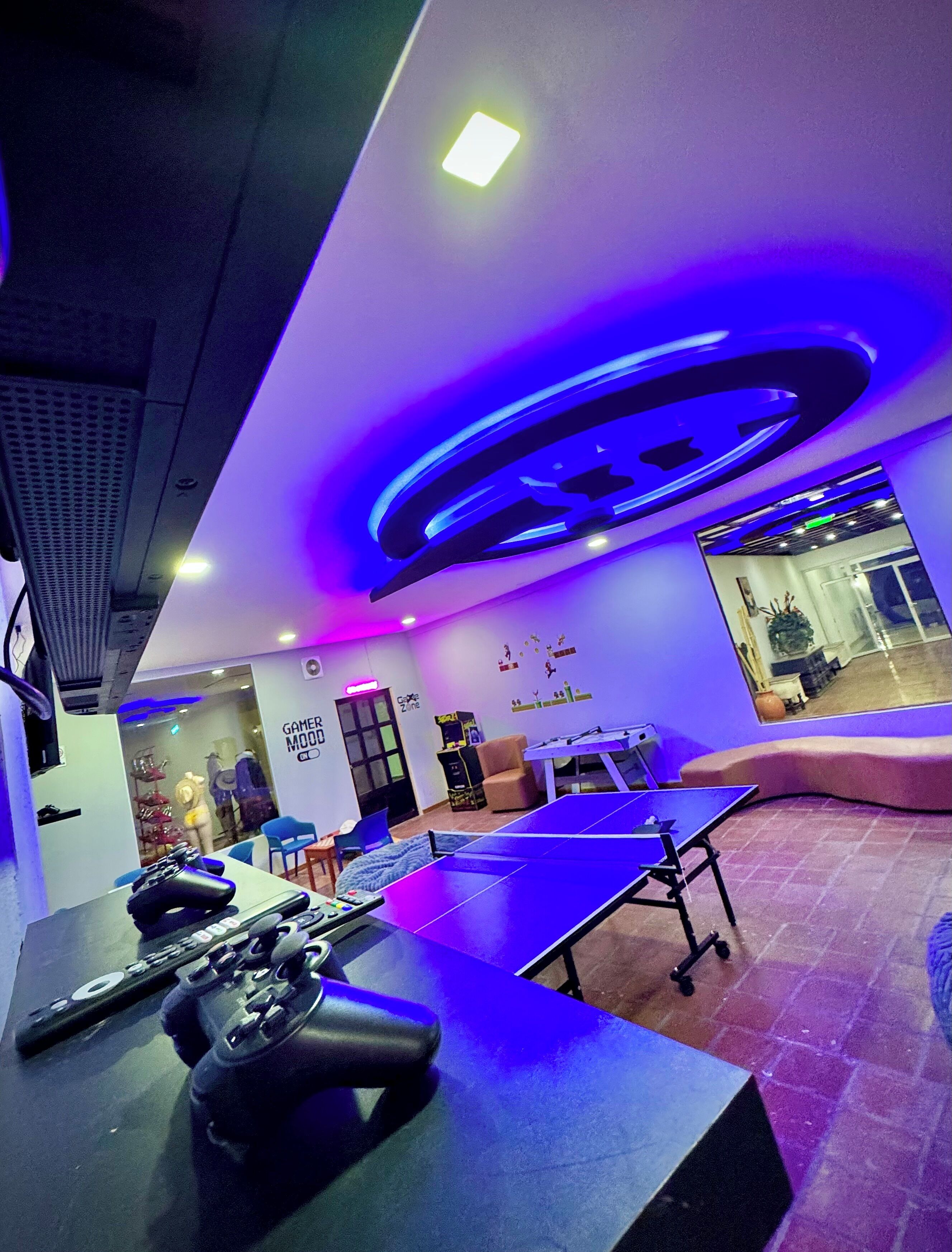A gaming room with a ping pong table, gaming consoles, and a wall with a 'GAMEDOME' sign.
