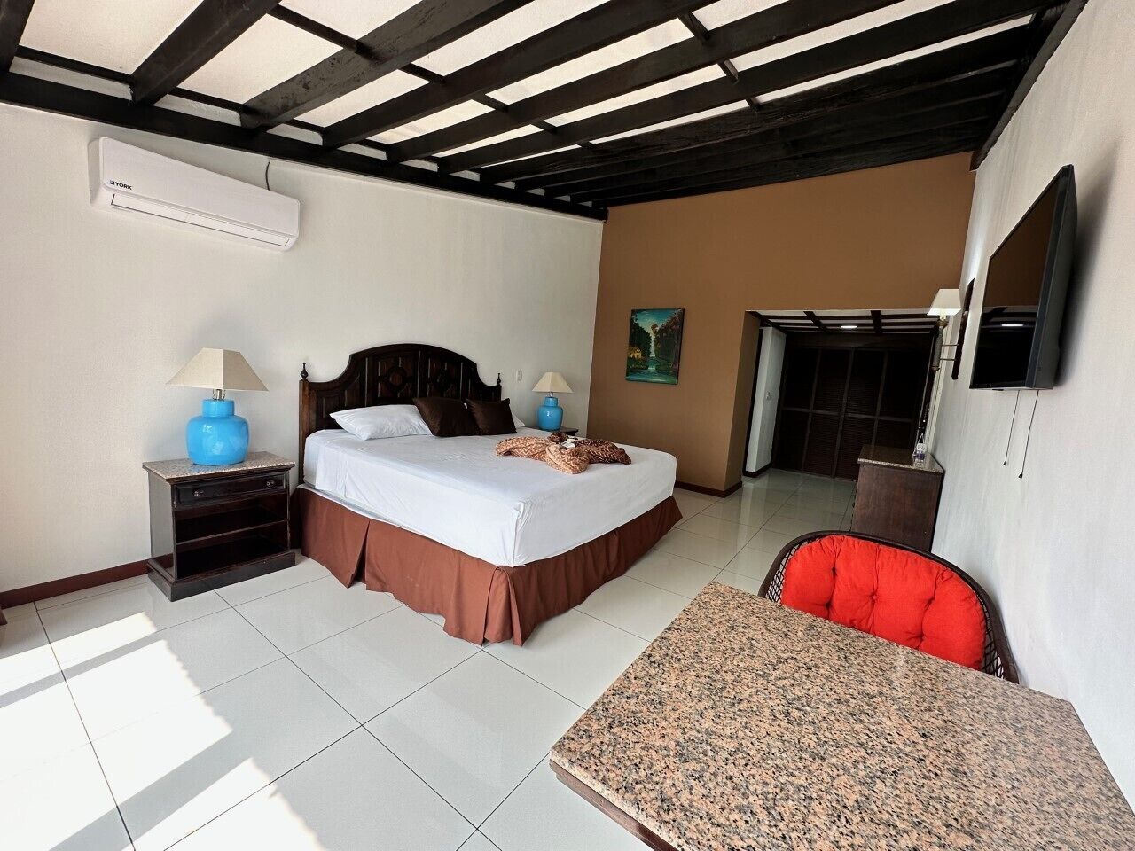 Habitación de hotel con cama, escritorio, silla, televisión y un cuadro en la pared.