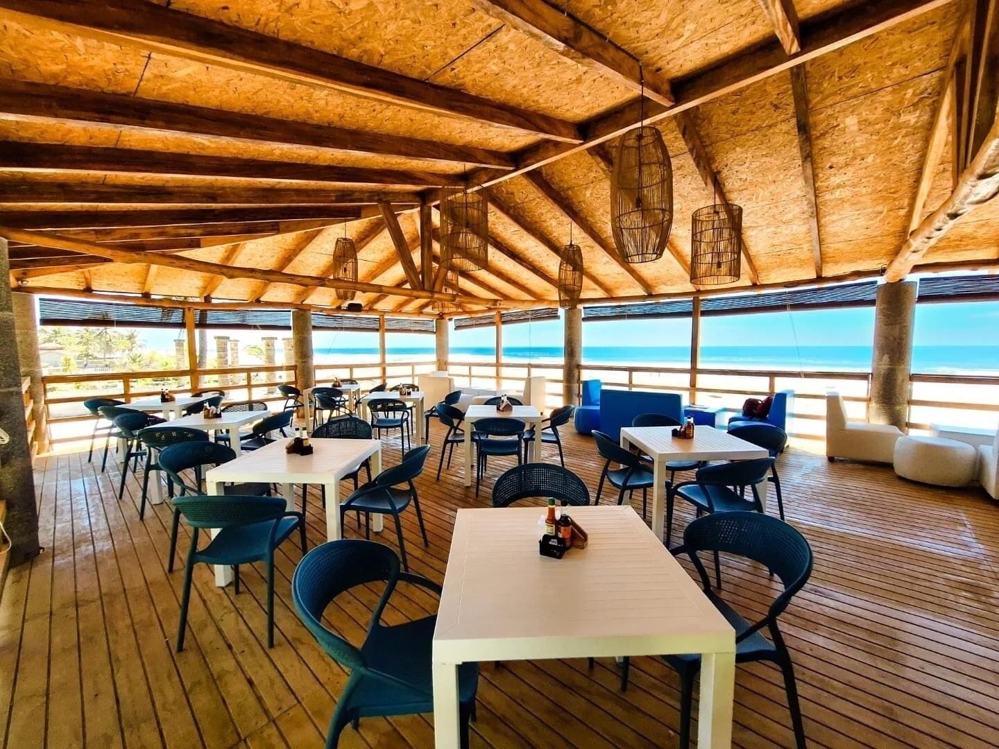 Ein Freiluft-Esbereich mit Holztischen und -stühlen mit Blick auf einen Strand.