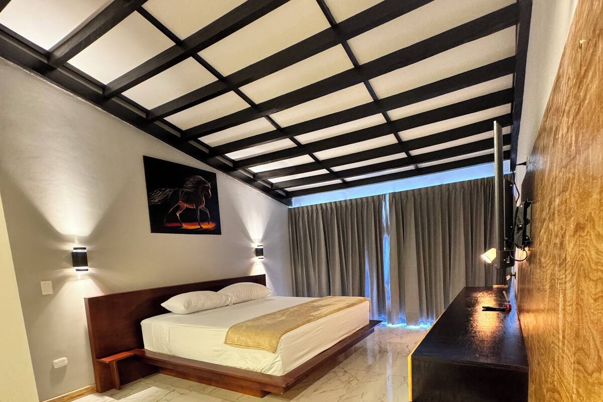 Ein modernes Hotelzimmer mit Bett, einem Bild an der Wand, einer Holzbank und Blick ins Freie durch ein Fenster.