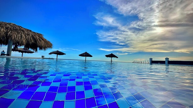 A swimming pool with a tiled floor and thatched umbrellas. - HOTEL TESORO BEACH (La Herradura)