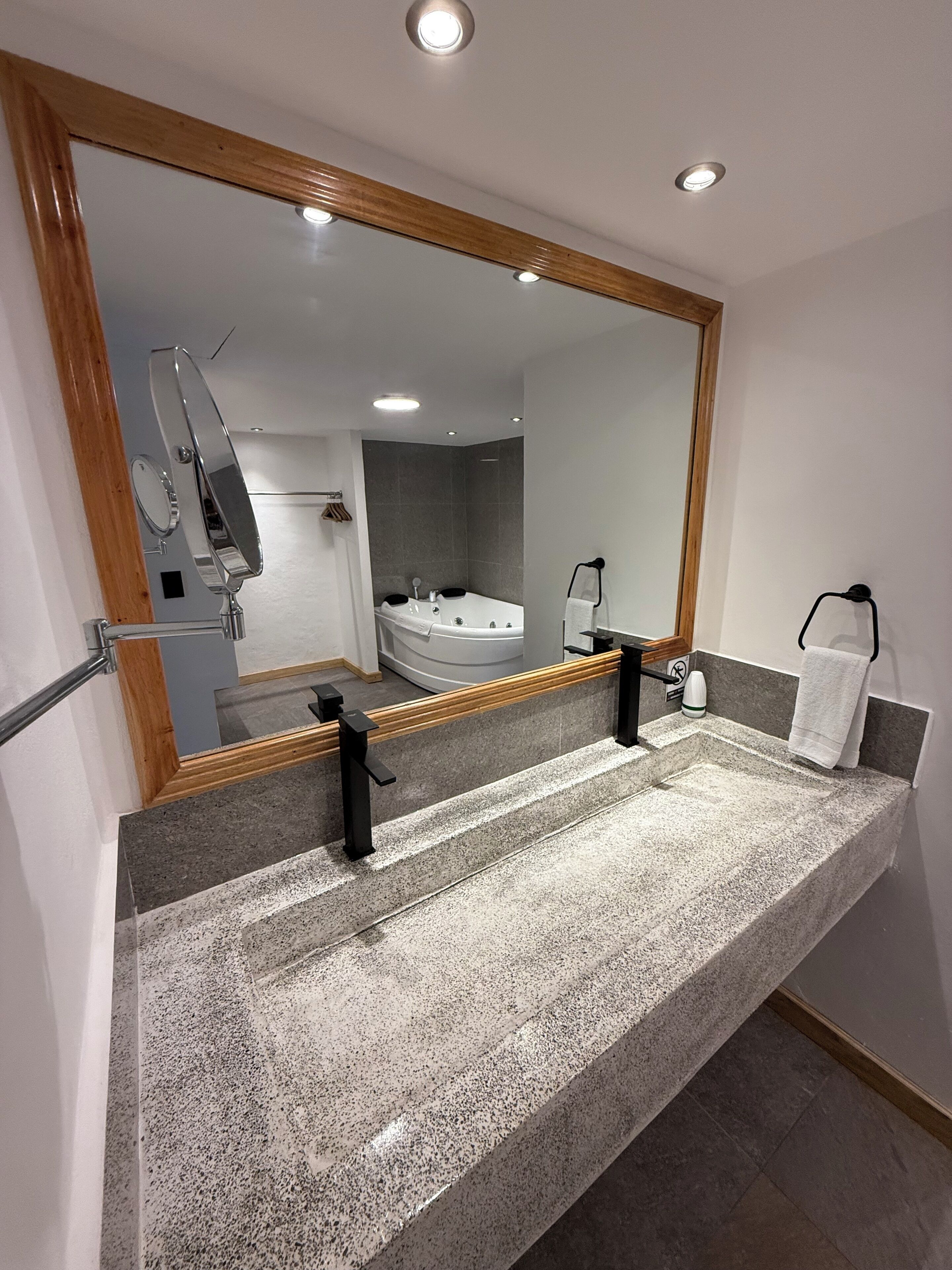 Een badkamer met een grote spiegel, een badkuip en een granieten aanrechtblad.