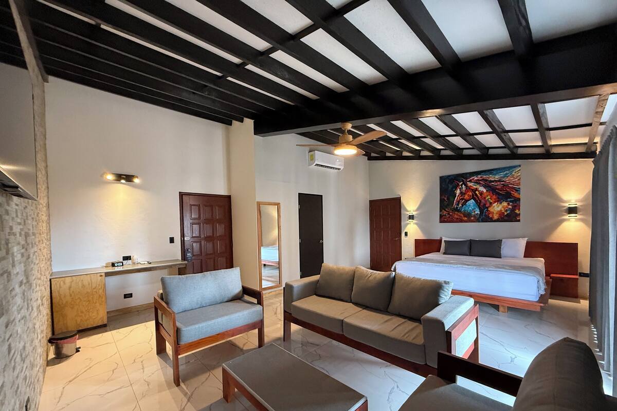 Ein modernes Hotelzimmer mit einem Bett, zwei Sofas, einem Couchtisch, einem Schreibtisch und einem Bild an der Wand.