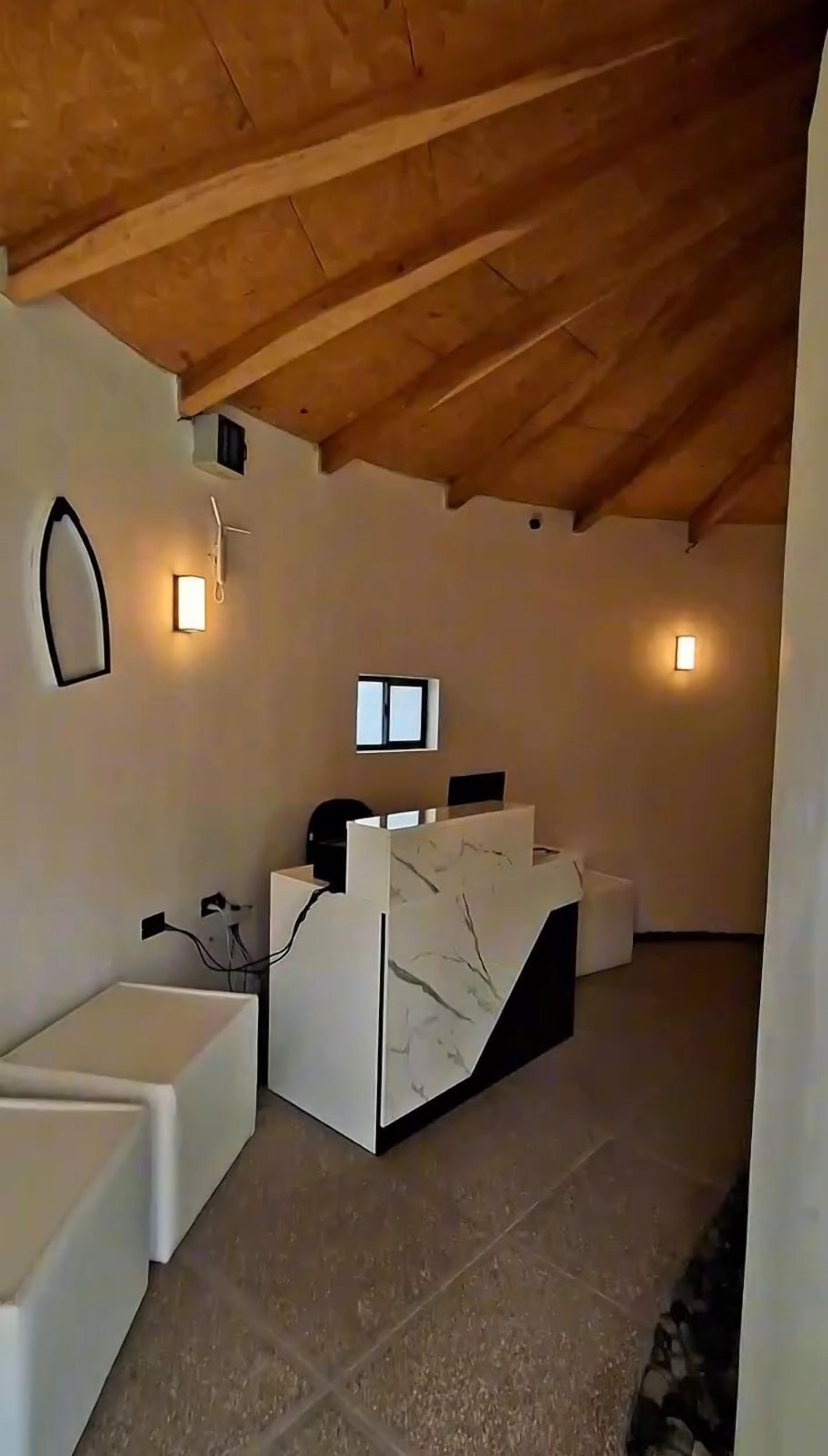 Un área de recepción con techo de madera, un mostrador de recepción, dos sofás blancos e iluminación empotrada en la pared.